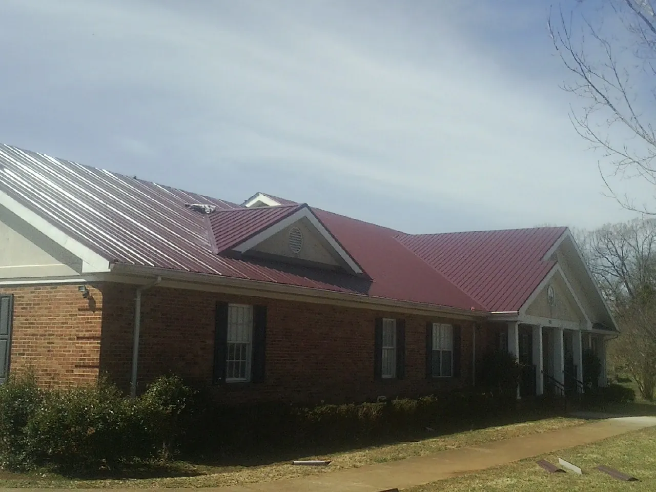 Red metal roof with gabled entries on a long brick building, from a Hail Damage Roof Repair job in Waterbury