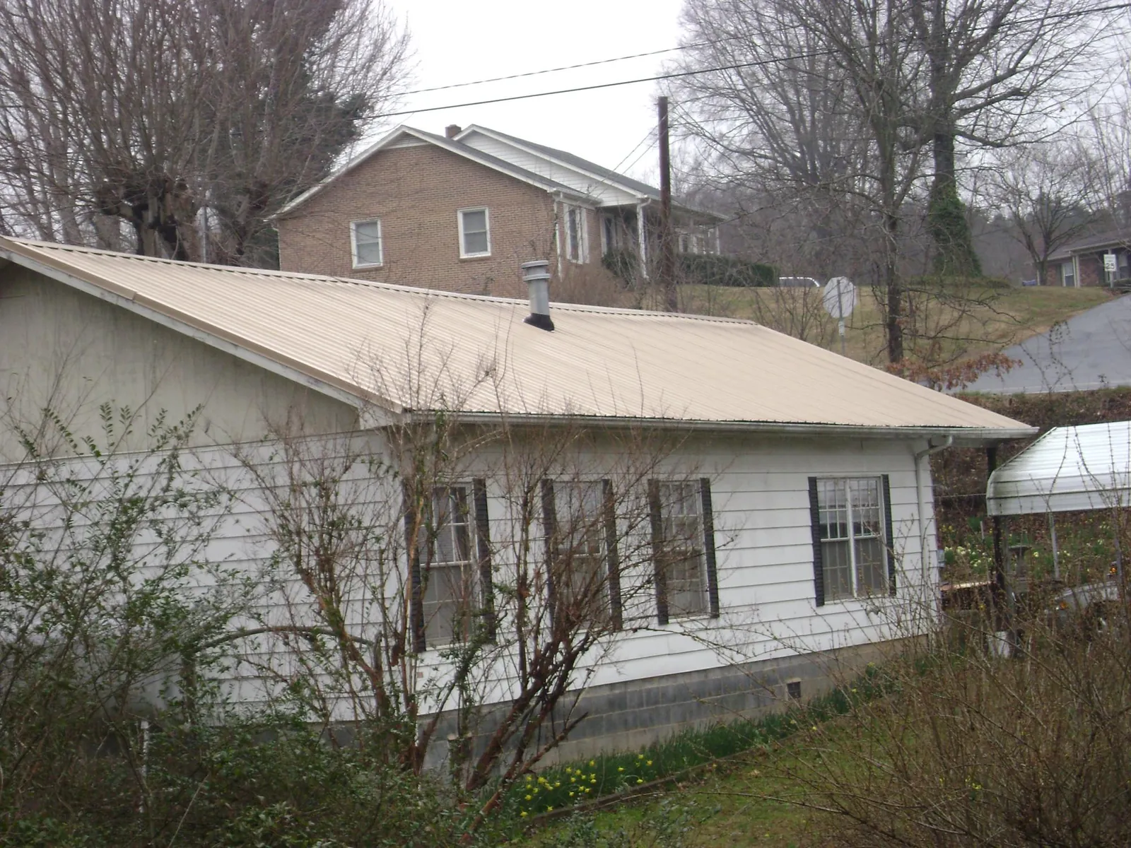 Tan metal roof on a white sided house set into a hillside — Commercial Roofing by Roofing Brothers in Waterbury