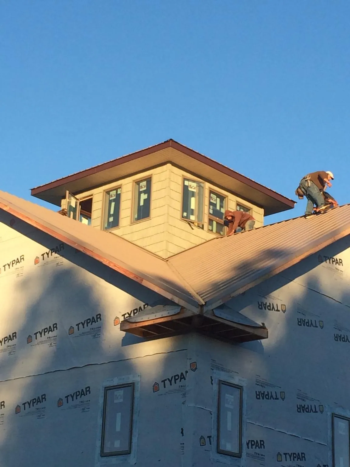 Roofers working around a rooftop cupola on a new metal roof at sunset — Roof Waterproofing in Waterbury by Roofing Brothers